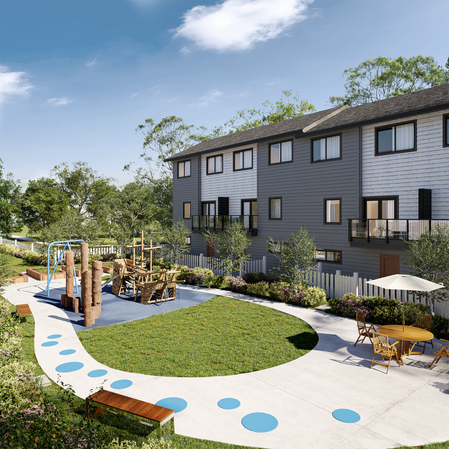 A landscaped courtyard beside three‑storey townhomes features a circular pathway, green lawn, and a wooden playground structure. Outdoor benches, tables with umbrellas, and trees create a shared community play and seating area.