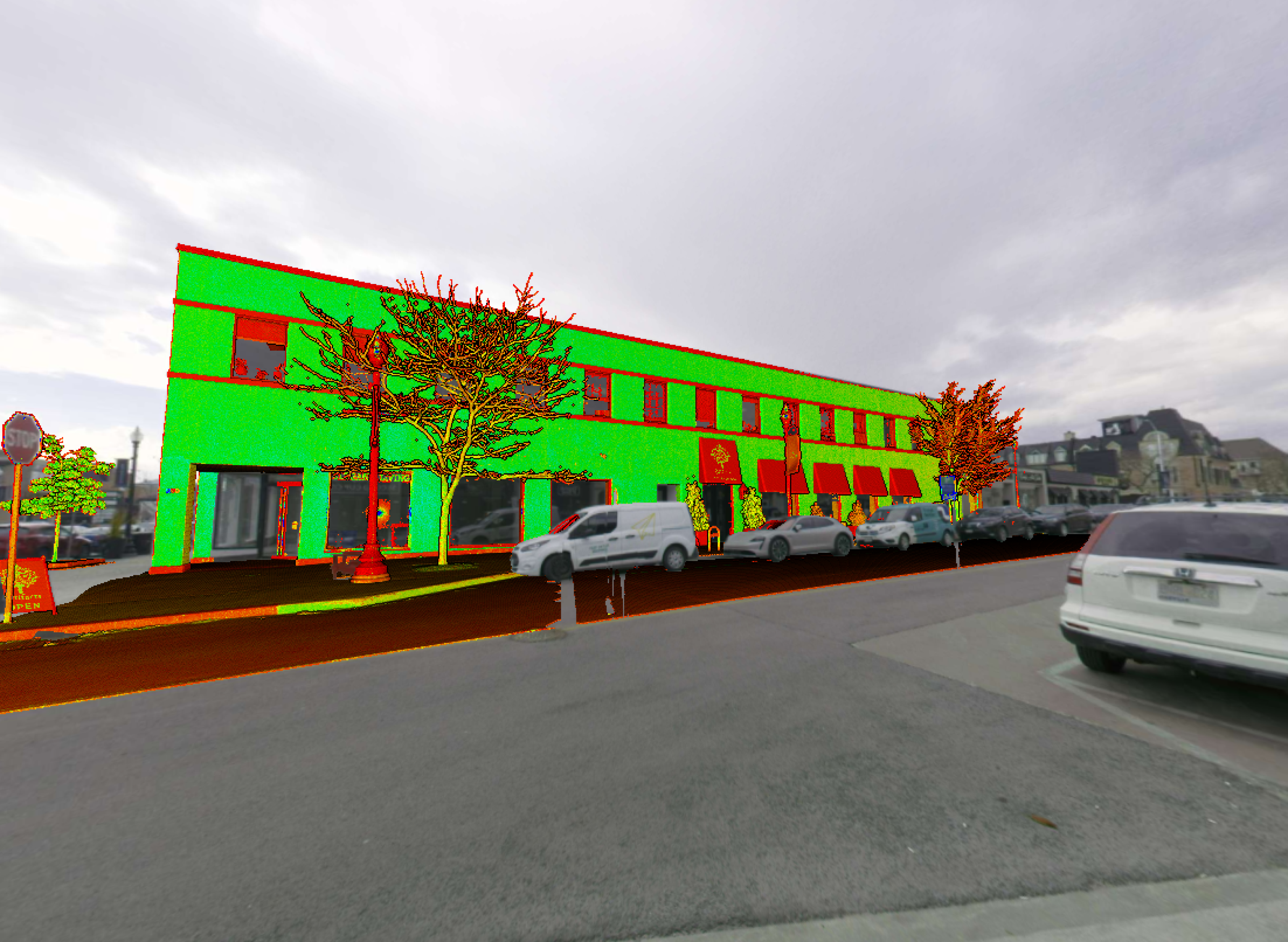 A color‑coded 3D scan visualization of a two‑storey commercial building along a city street. The facade appears highlighted in green and red, with parked cars, trees, and surrounding sidewalks visible.
