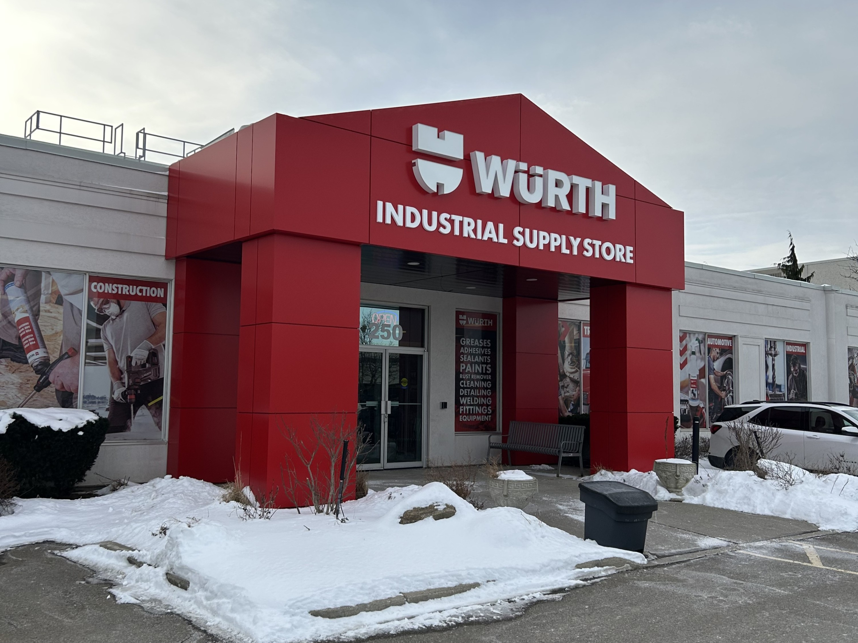 A Würth Industrial Supply Store exterior with a bold red entrance structure and white signage. Snow covers the ground around the building, with product graphics on the walls and parked vehicles visible nearby.