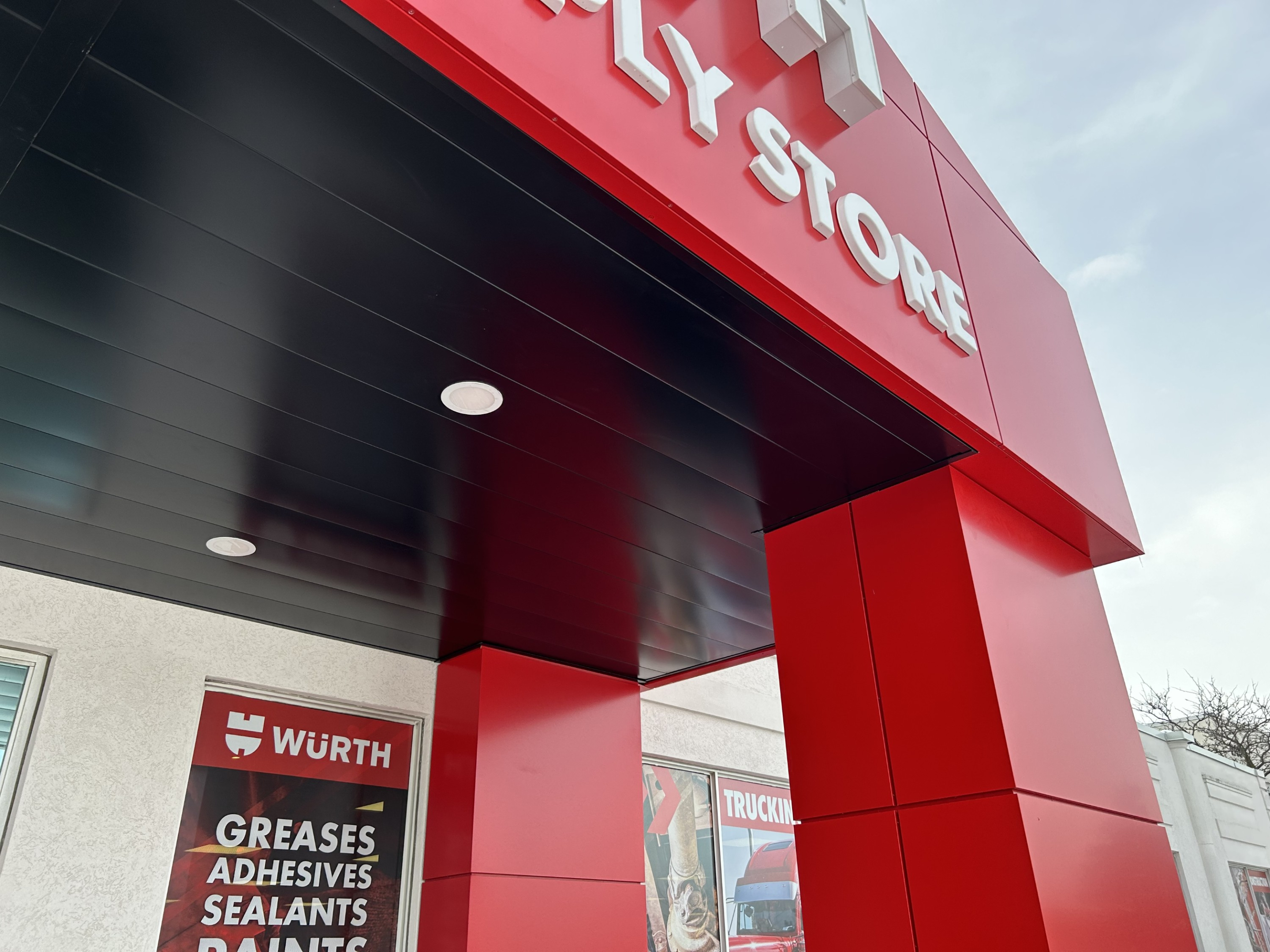 A close-up view of the Würth Industrial Supply Store entrance showing a bold red canopy and support columns. Product signage and promotional graphics are visible on the wall beneath the covered entry.