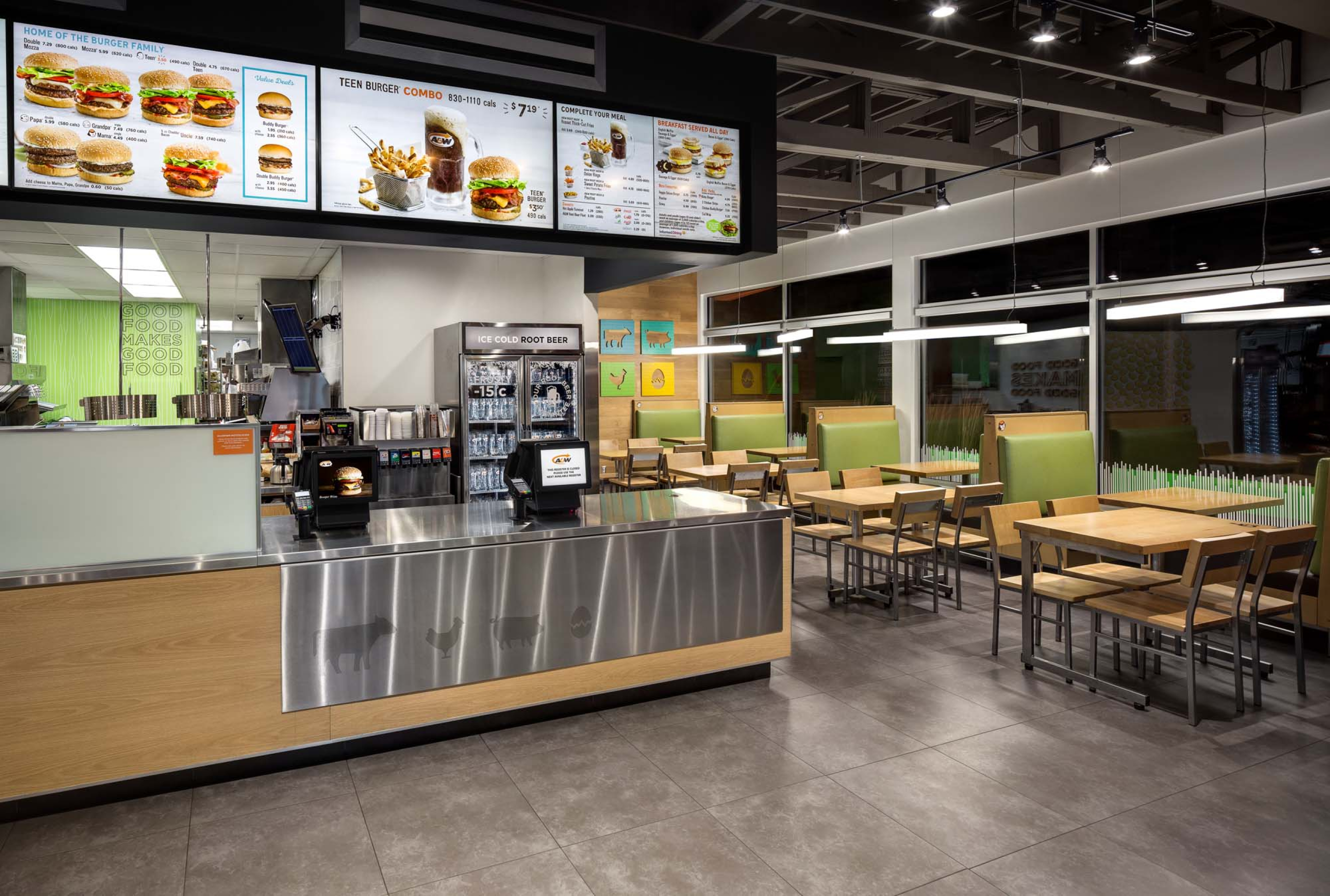 Modern fast‑food restaurant interior with a service counter, illuminated menu boards, and stainless‑steel fixtures, alongside clean seating areas with tables and green booth seating under bright overhead lighting.