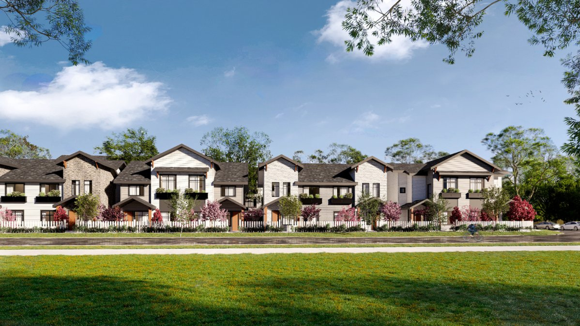 A rendered view of a row of modern two‑storey townhomes with light siding, dark roofs, and small front porches. Landscaped trees, flowering plants, a white fence, and a grassy foreground line a residential street under a clear sky.